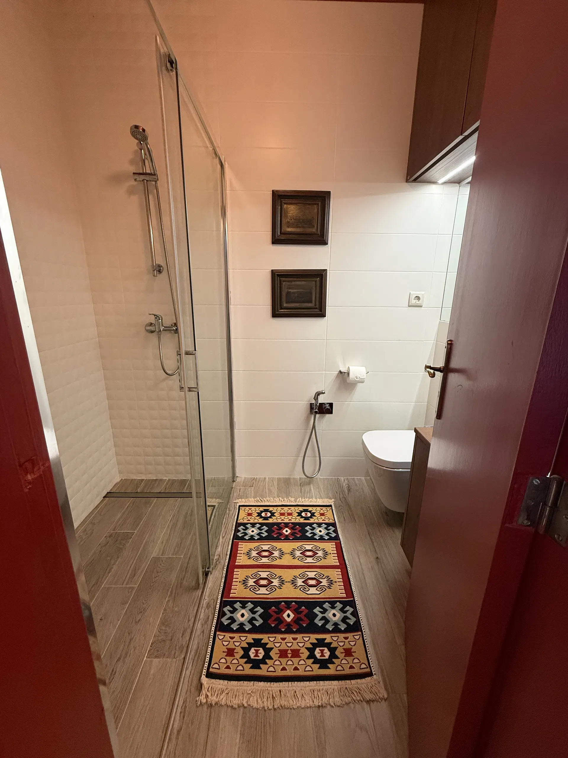 Casa de banho com duche envidraçado, lavatório e tapete de padrão colorido.