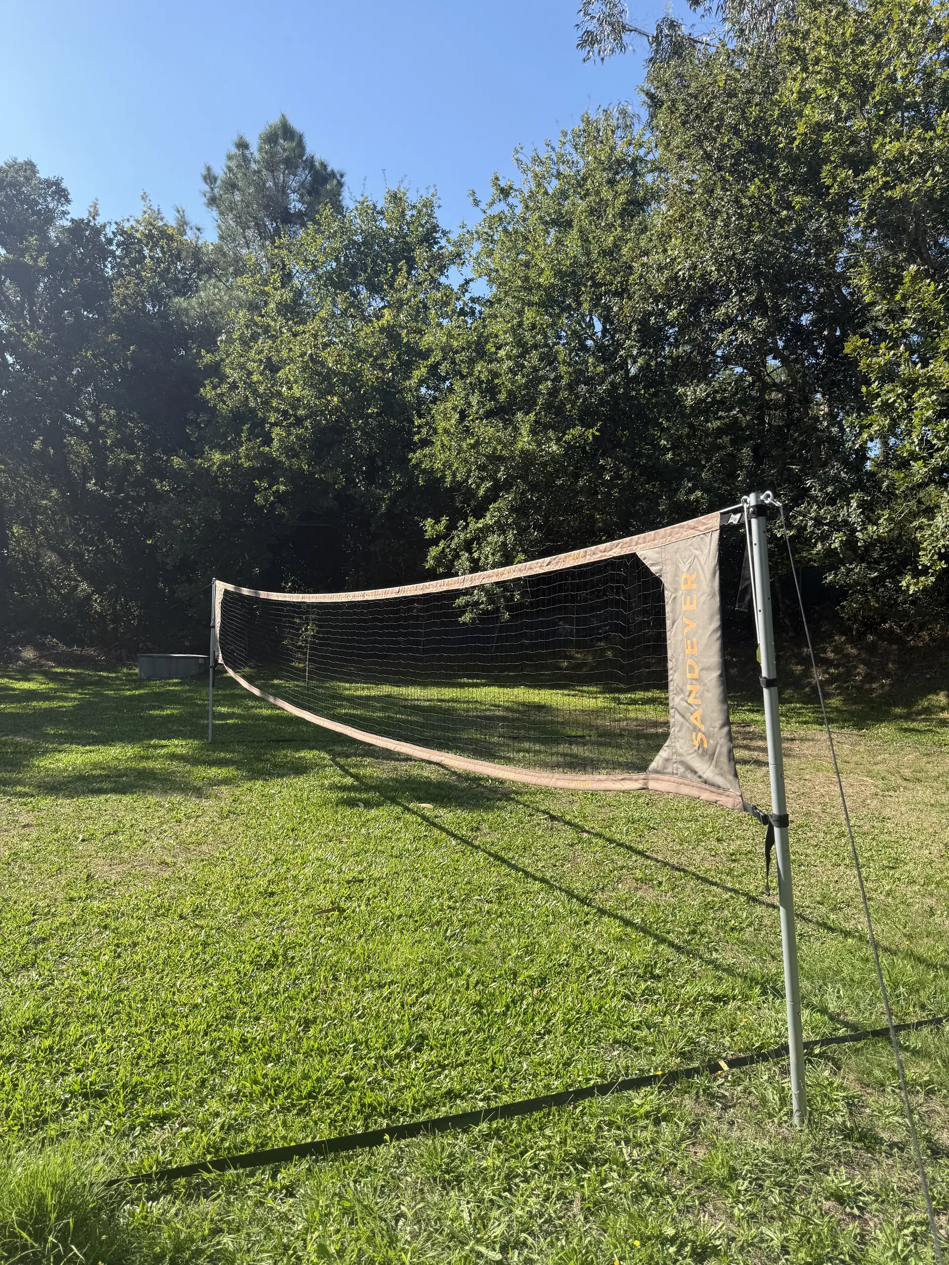Rede de badminton montada no relvado, rodeado de árvores.