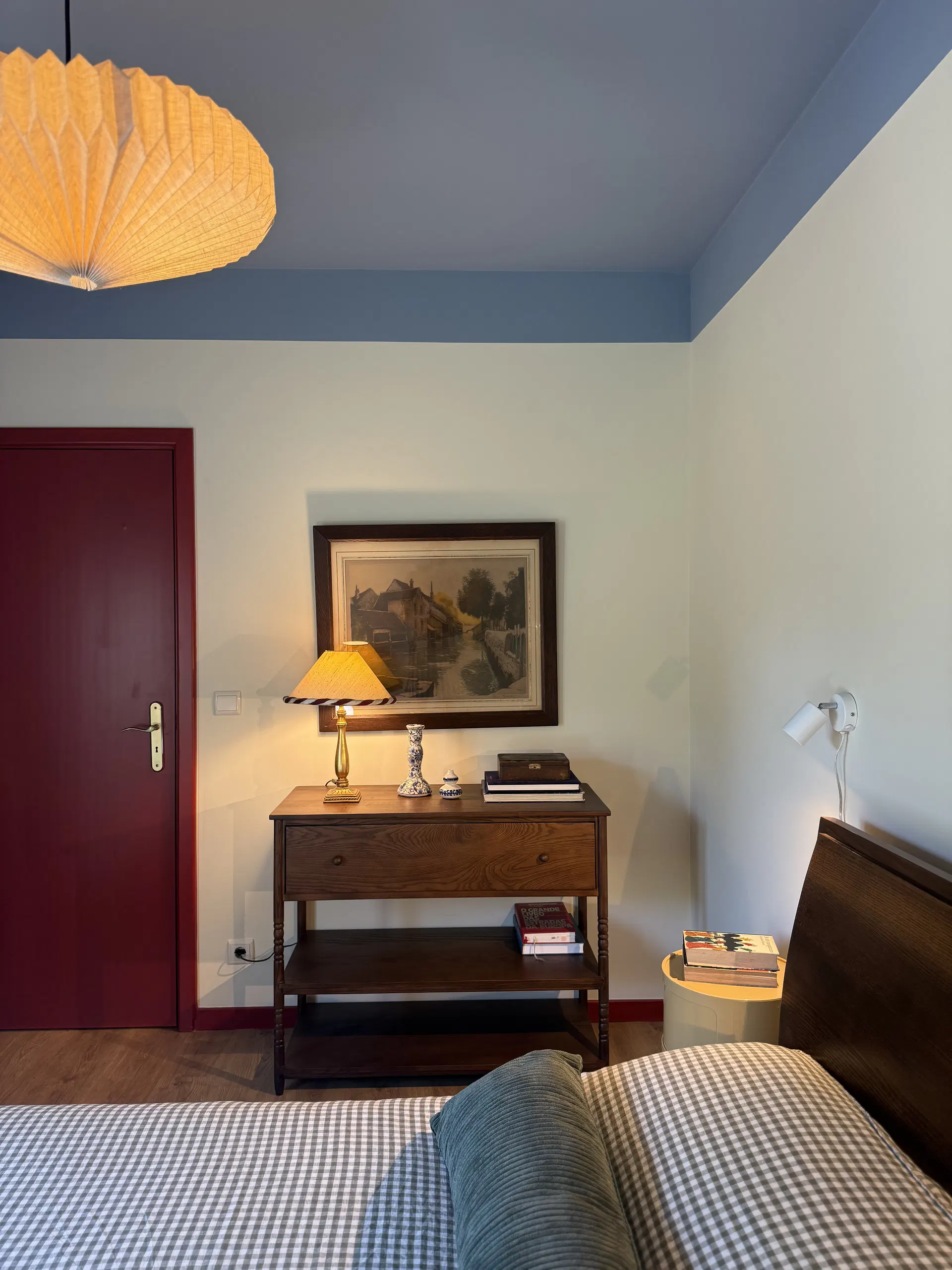 Consola de madeira, quadro e candeeiro junto à cama no quarto azul.