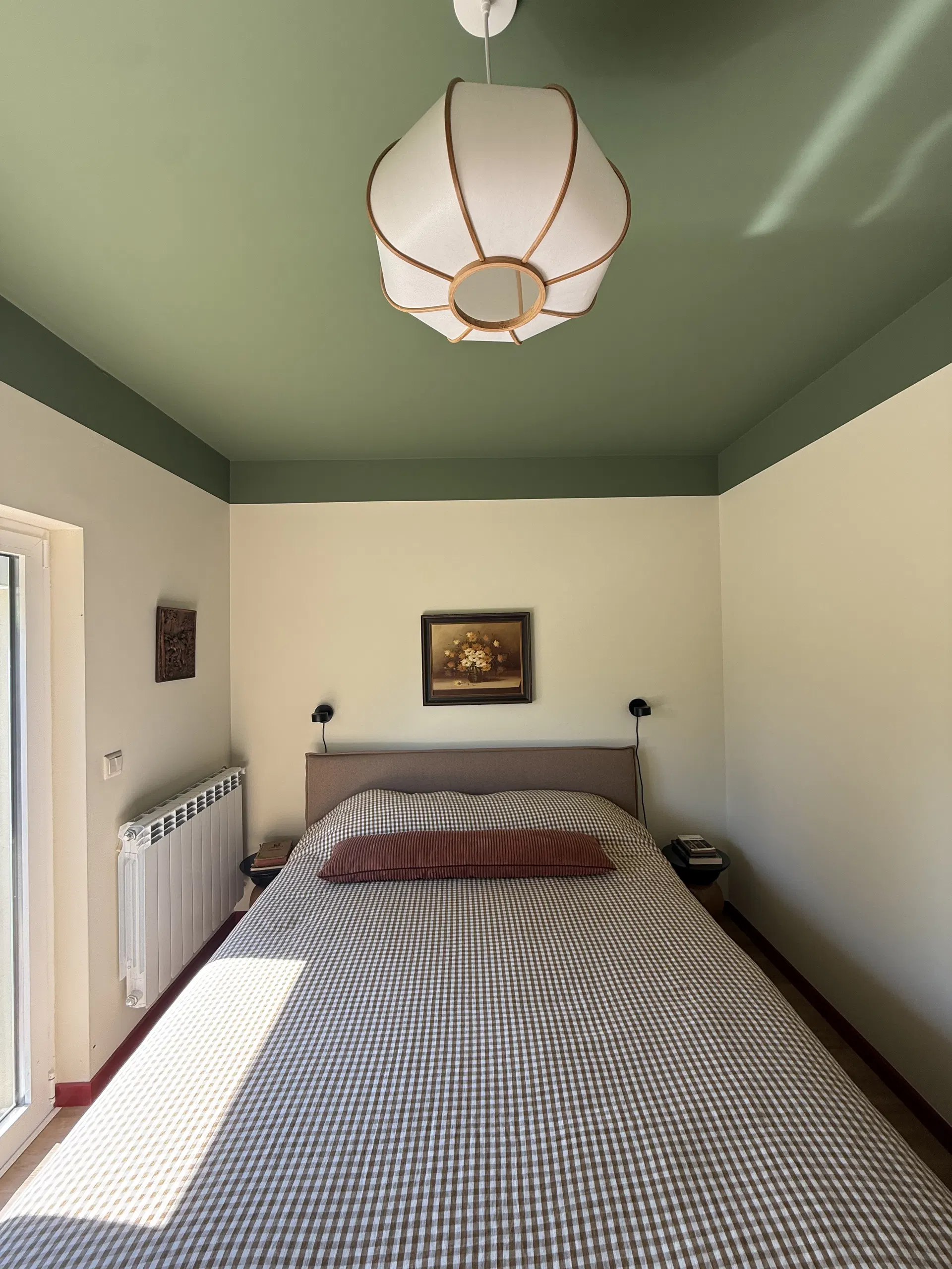 Quarto de casal com teto verde, candeeiro de papel e colcha às riscas.