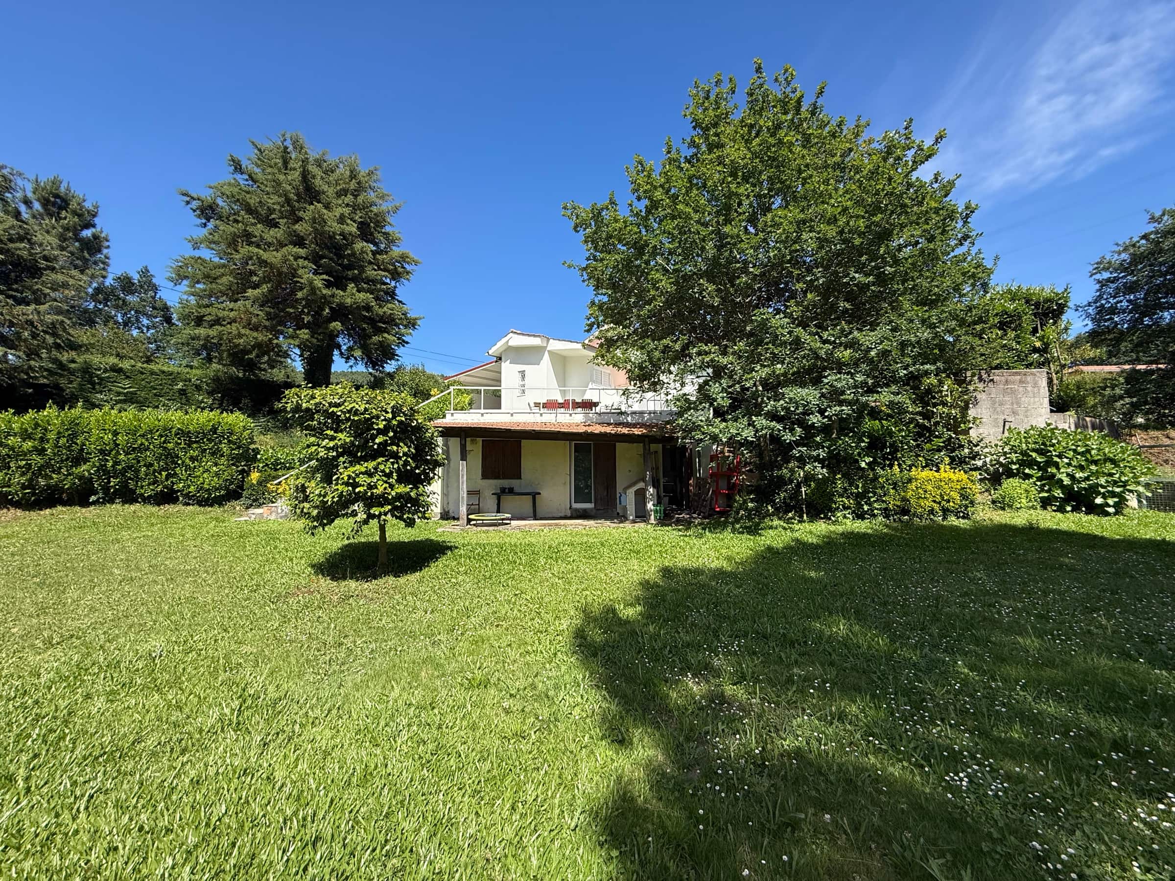 A Casa de Santa Eulália vista do relvado: dois pisos brancos com varanda e um alpendre de telha aberto para o jardim.