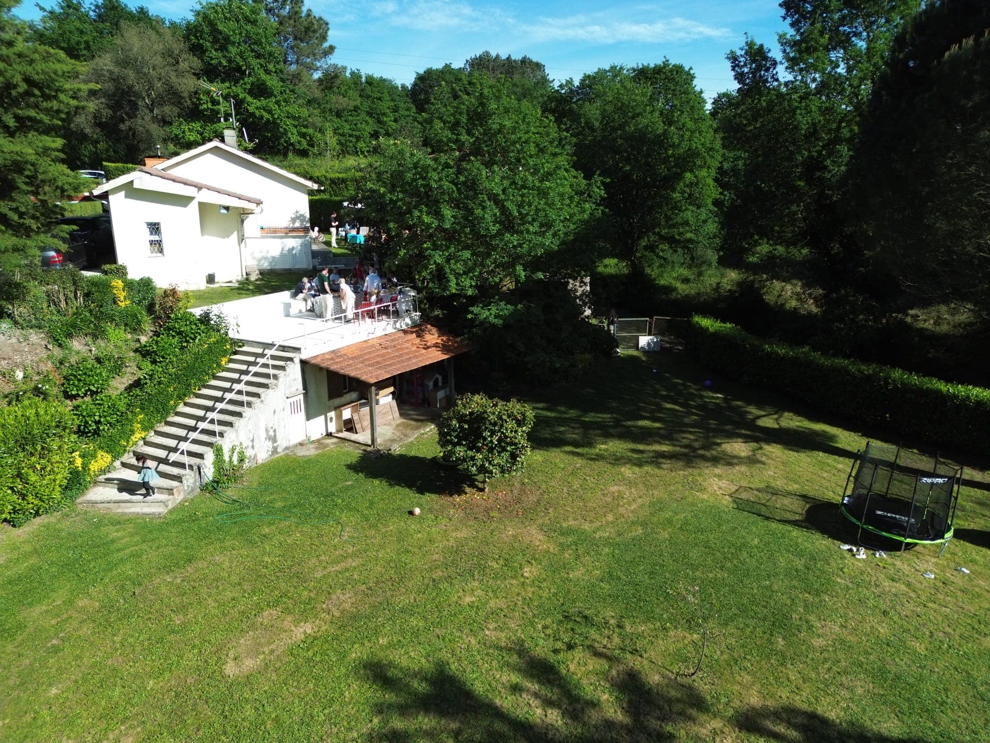 A casa e o terraço vistos do ar, com a escadaria a descer para o relvado grande, entre árvores.
