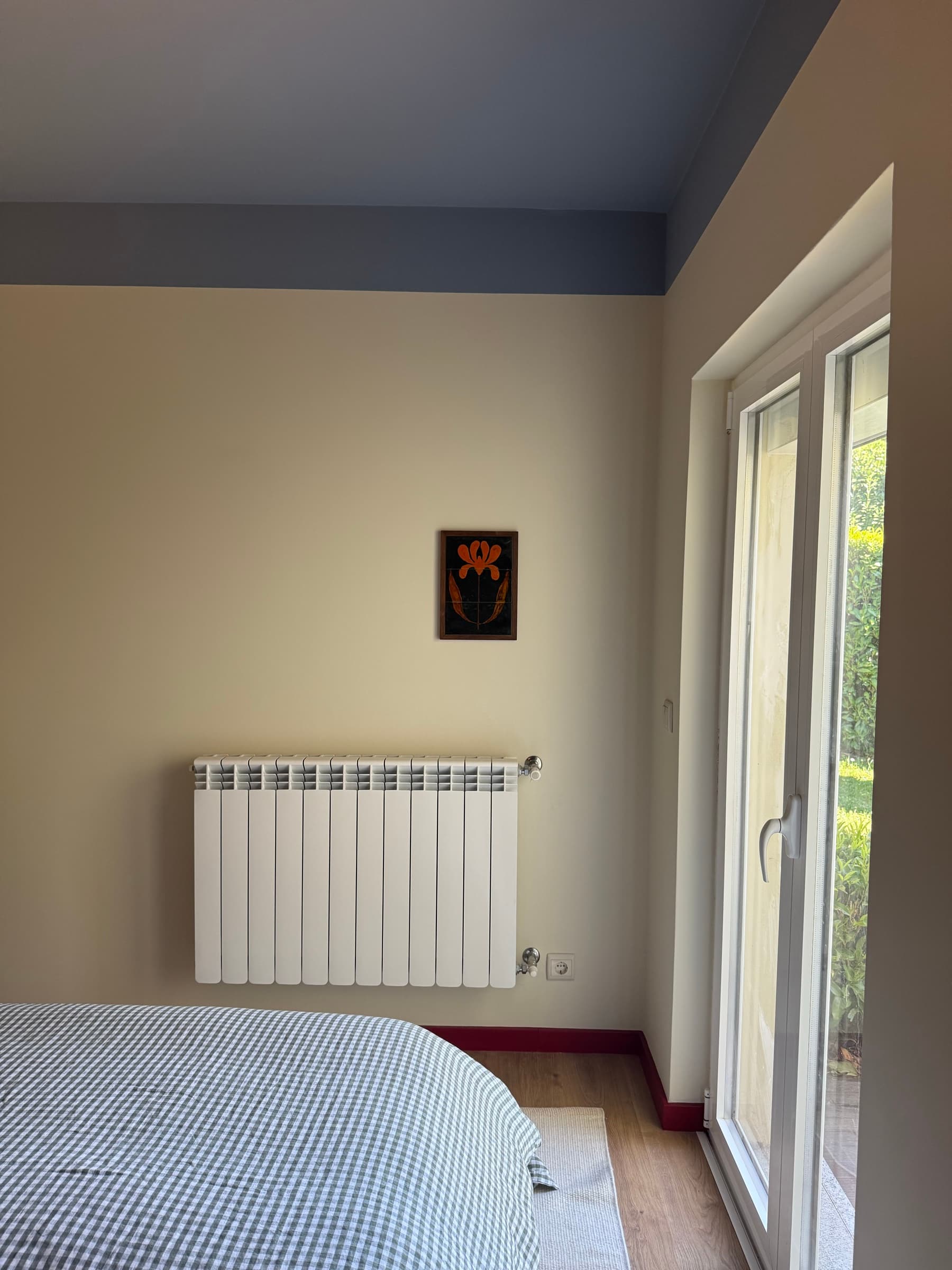 Quarto com teto azul e porta de vidro para o jardim; o radiador na parede diz que o inverno também é bem-vindo.