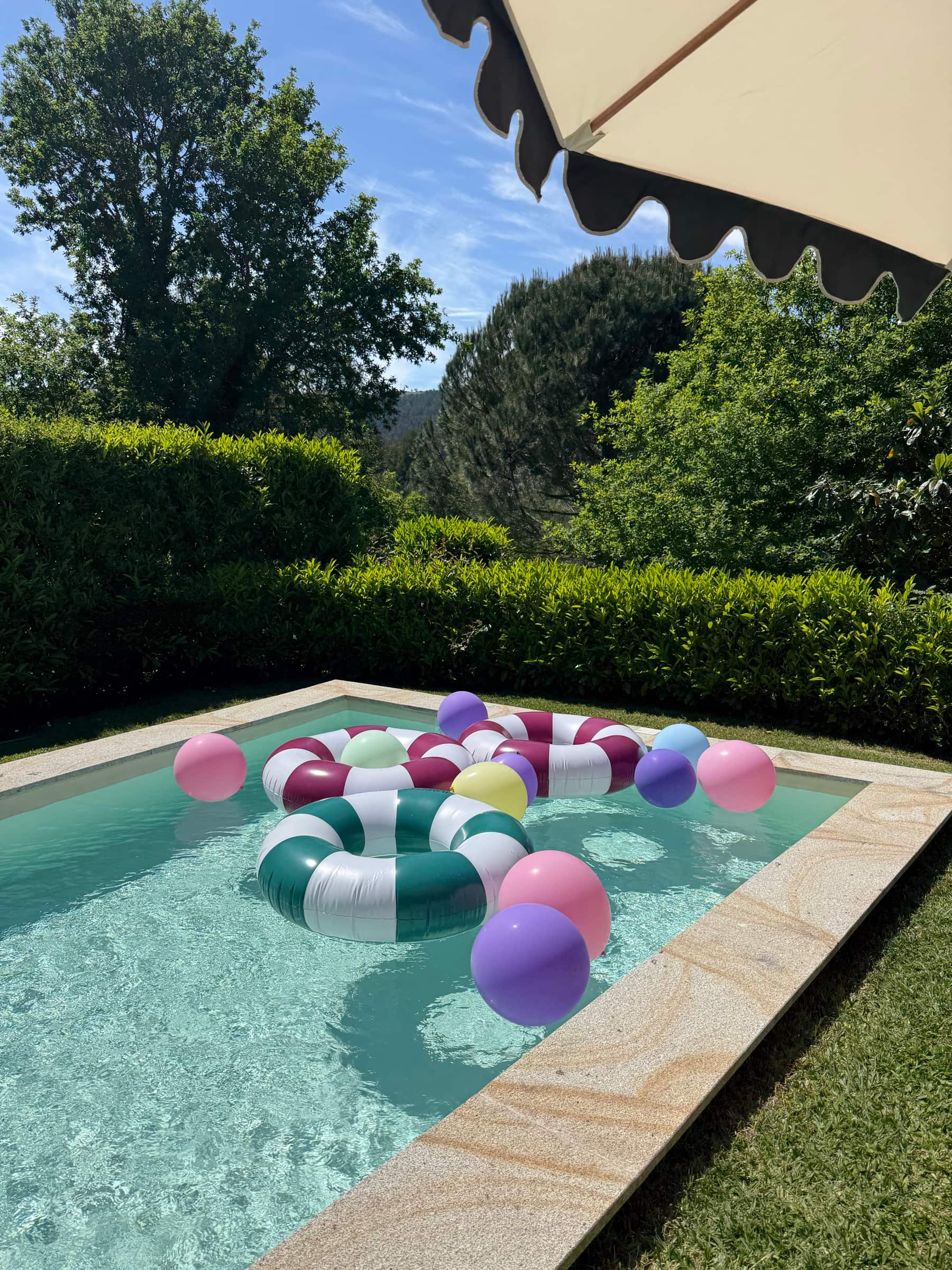 Boias coloridas na piscina, com a sebe alta e os montes do Minho ao fundo.