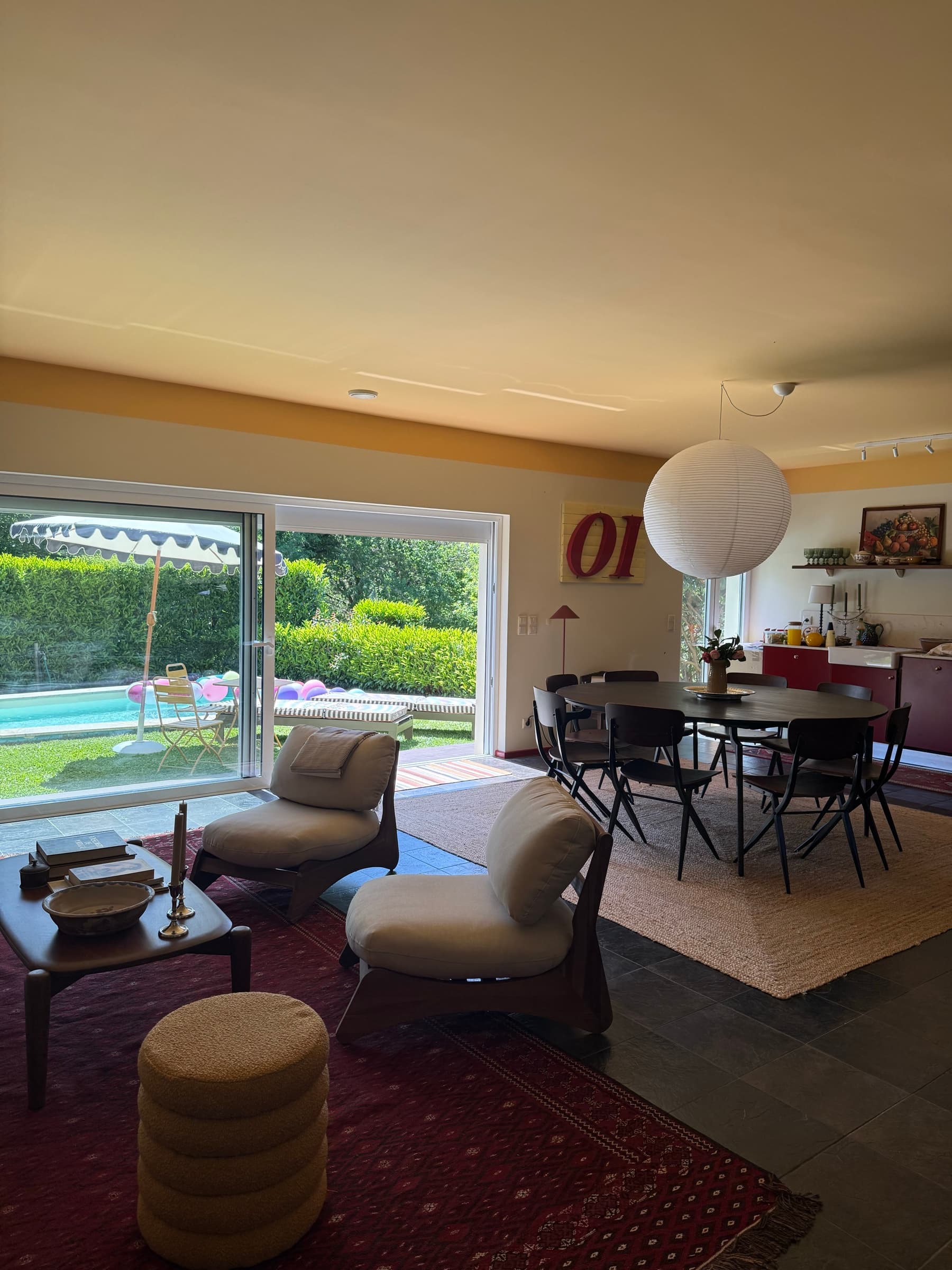 A sala em espaço aberto: zona de estar, mesa de jantar e a cozinha vermelha ao fundo, com a piscina à vista pelas portas de correr.